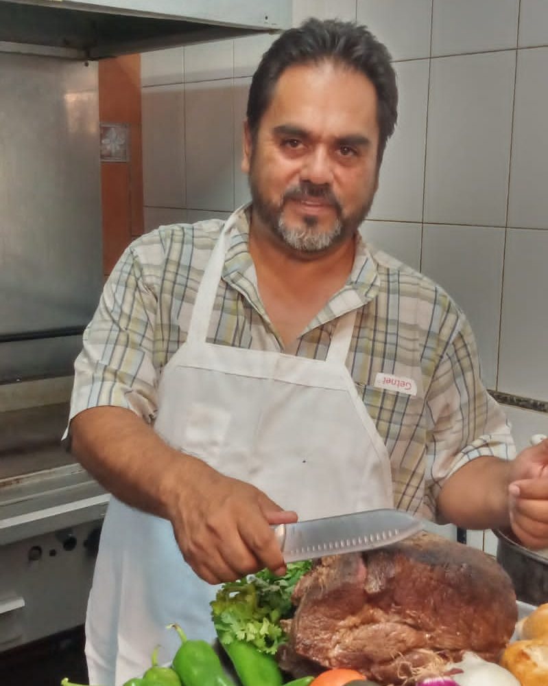 Cocinero de Tortería Los Azulejos rebanando la pierna horneada junto a chiles, jitomate y aguacate